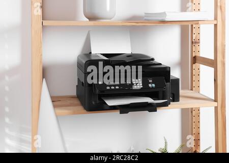 Moderner Drucker mit Papier auf Holzregal im Home Office Stockfoto