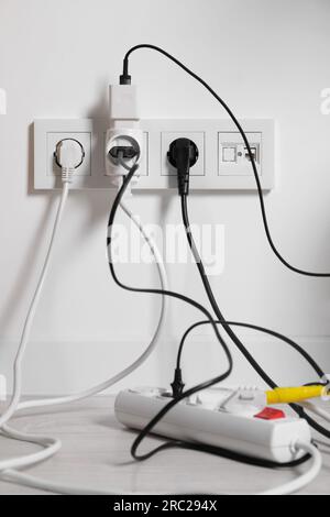 Verschiedene elektrische Stecker in Steckdose und Steckdosenleiste auf dem Boden im Innenbereich Stockfoto