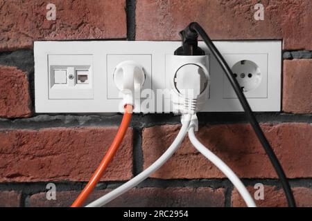 Viele verschiedene elektrische Netzstecker in Steckdosen an roten Ziegelwänden Stockfoto