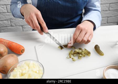 Eine Frau schneidet eingelegte Gurken auf einem weißen Holztisch, Nahaufnahme. Ich koche Vinaigrette-Salat Stockfoto