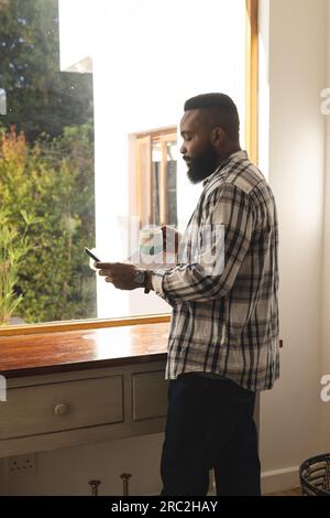 Ein afroamerikanischer Mann mit kariertem Hemd, einer Tasse Kaffee und einem Smartphone Stockfoto