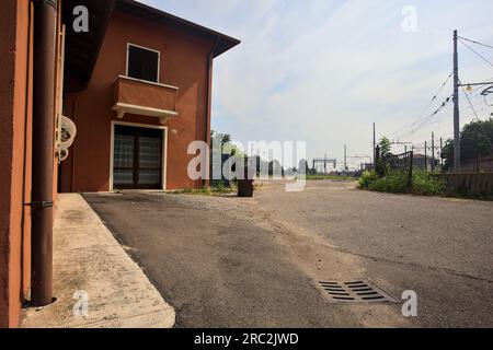 Gepflasterte Straße neben Bahngleisen und ein Bahnhof in der Ferne an einem sonnigen Tag in einer italienischen Stadt Stockfoto