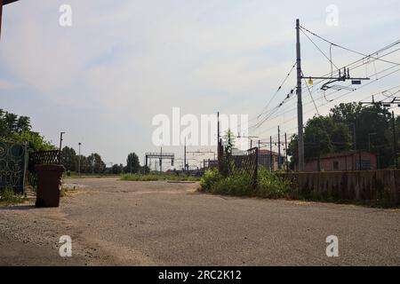 Gepflasterte Straße neben Bahngleisen und ein Bahnhof in der Ferne an einem sonnigen Tag in einer italienischen Stadt Stockfoto