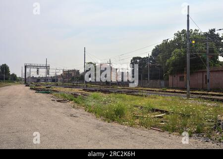 Gepflasterte Straße neben Bahngleisen und ein Bahnhof in der Ferne an einem sonnigen Tag in einer italienischen Stadt Stockfoto