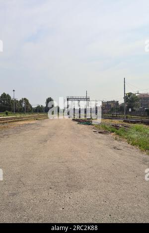 Gepflasterte Straße neben Bahngleisen und ein Bahnhof in der Ferne an einem sonnigen Tag in einer italienischen Stadt Stockfoto