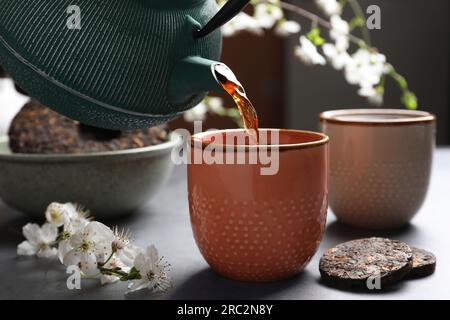 Frisch gebrühten pu-erh-Tee in eine Tasse auf einem grauen Tisch gießen, schließen Stockfoto