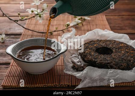 Frisch gebrühten pu-erh-Tee in eine Tasse auf einem Holztisch gießen, schließen Stockfoto