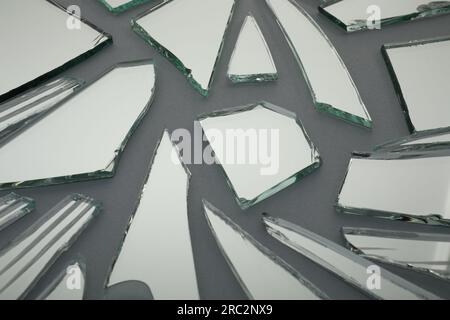 Scherben von zerbrochenem Spiegel auf grauem Hintergrund, Nahaufnahme Stockfoto