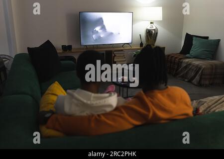 Ein afroamerikanisches Paar in Socken, das sich zu Hause entspannt und einen gruseligen Film ansieht Stockfoto