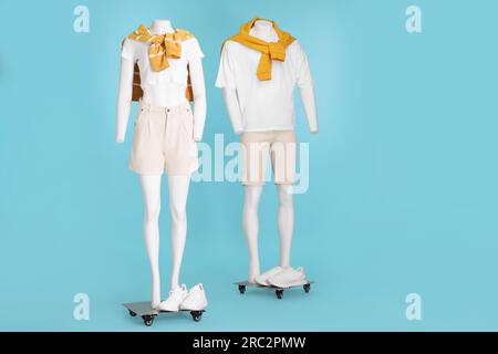 Schaufensterpuppen mit Turnschuhen in weißen T-Shirts, Shorts und orangefarbenen Pullover auf hellblauem Hintergrund. Stylische Outfits für Männer und Frauen Stockfoto