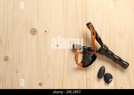 Schwarze Steinschleuder mit Steinen auf Holztisch, flach liegend. Platz für Text Stockfoto