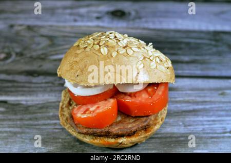 Scharfer gebratener Rindfleischburger, gekocht in einem kochenden, flachen Öl mit Scheiben von Tomaten und Zwiebeln in einem Haferbrötchen garniert mit Hafer und Sesam, Fast Food Stockfoto