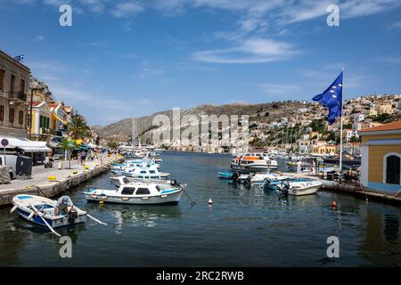 Symi, Griechenland - 30. Mai 2023: Blick auf die Hafenbucht auf der Insel Symi, mit bunten kleinen Booten und traditioneller griechischer Architektur. Stockfoto