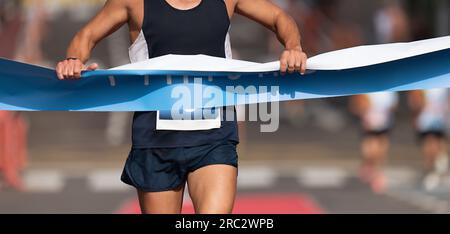 Ein Mann läuft auf die Ziellinie zu, ein männlicher Läufer gewinnt das Rennen im Freien in der Stadt. Gewinnt die Ziellinie Stockfoto