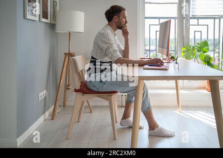 Junger Freiberufler mit Rückenstütze, der am Tisch sitzt und den Computer benutzt Stockfoto