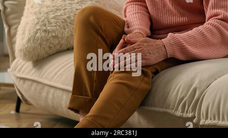 Kaukasisch krank ungesund leiden alte Frau zu Hause Couch ältere Frau leiden an Knieschmerzen Schmerzen Seniorenpensionierte Frau Oma fühlt sich schlecht verletzt Stockfoto