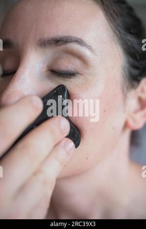 Junge Weiße, die eine Gesichtsbehandlung bekommt. Therapeut macht Hautkratztechnik. Chinesische Technik, Gua sha, zur Schmerzlinderung und -Behandlung Stockfoto