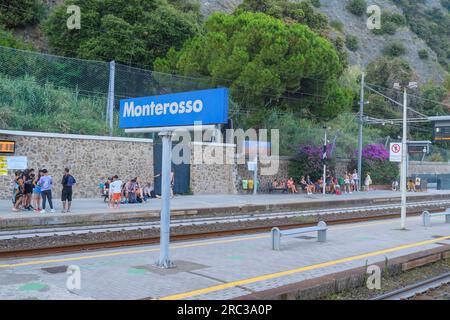 Juni 2023 Monterosso, Italien: Monterosso-Schild auf dem Bahnsteig gegenüber den Zügen, der Bahnhofsinfrastruktur und Fahrgästen mit Koffern Stockfoto