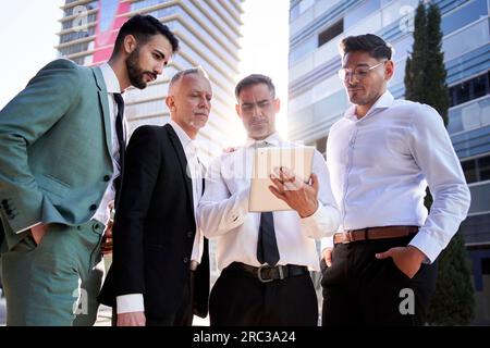 Ein Team aus verschiedenen männlichen Profis konzentriert sich auf das Tablet des Teamleiters. Kollegen meinen es ernst. Stockfoto