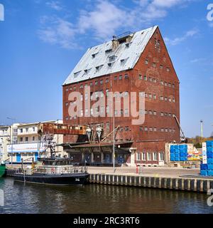 Kolberg, Polen, 20. April 2023: Historisches Lagersilo aus rotem Backstein mit Kai und Schiff im Hafen der polnischen Stadt Kołobrzeg Stockfoto