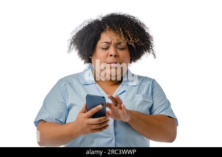 Porträt einer jungen Afro-Latina-medizinischen Frau in blauer Uniform überrascht durch Telefonlesemeldungen, weißer Hintergrund mit Kopierbereich. Stockfoto