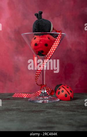 Ein dreieckiges Glas enthält einen gefüllten Marienkäfer und eine Marienkäfer-Geldbörse daneben Stockfoto