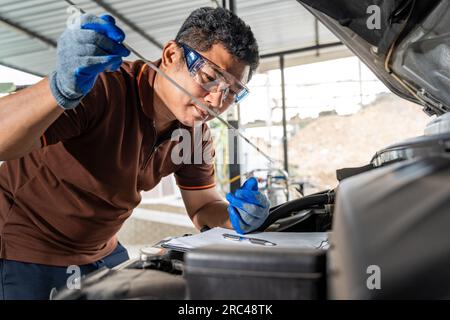 Ein asiatischer Automechaniker, der das Autoöl überprüft und das Auto in seiner Werkstatt repariert Stockfoto