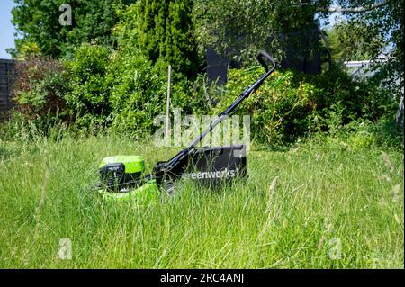 Ein Greenworks Rasenmäher, der nach dem Mähen einen Rasen mäht, kann bei langem Gras den Rasen mähen. Stockfoto