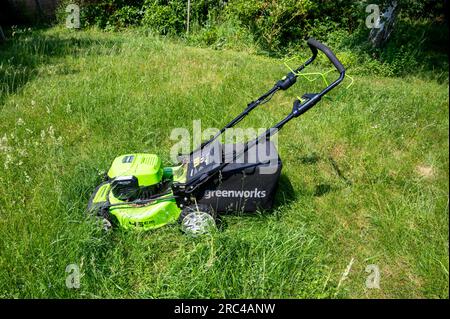 Ein Greenworks Rasenmäher, der nach dem Mähen einen Rasen mäht, kann bei langem Gras den Rasen mähen. Stockfoto