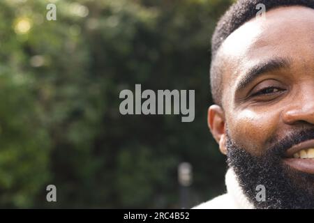 Porträt eines glücklichen afroamerikanischen Mannes mit kurzen Haaren, der im Garten einen weißen Pullover trägt Stockfoto