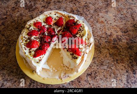 Hausgemachter Pavlova auf einem Teller, bei dem eine Portion fehlt und auf einer gesprenkelten Arbeitsplatte sitzt Stockfoto