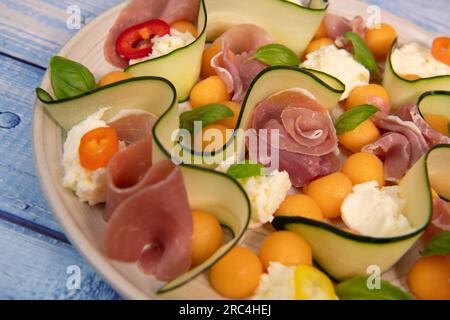 REZEPT FÜR MELONE, MOZARELLA, BASILIKUM UND GERÄUCHERTEN SCHINKENSALAT, GURKENSCHEIBE, ORANGENVINAIGRETTE Stockfoto