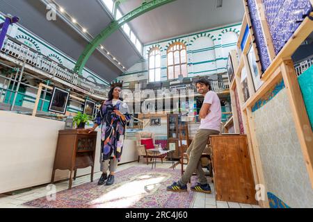 Birmingham, Großbritannien. 12. Juli 2023. Ein Swimmingpool aus dem Jahr 1907 ist die Heimat einer vorübergehenden Umwandlung in ein Wohnzimmer. Das Balsall Heath Gala Pool in der Innenstadt von Balsall Heath, Birmingham, bietet Kunstwerke, Teppiche und weiche Möbel, die einen willkommenen Ort für eine Tasse Tee und ein Gespräch bieten. Die Bäder der Moseley Road werden zur gleichen Zeit renoviert, um ihre edwardianischen Armaturen und Armaturen zu präsentieren. Die Koproduzenten des Projekts Danielle Marshall und Tim Hodgson inspizieren einen der drei Wohnräume. Kredit: Peter Lopeman/Alamy Live News Stockfoto