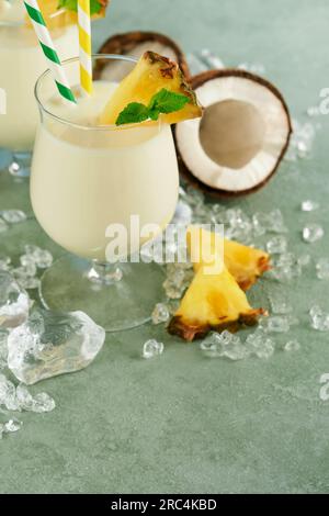 Pina Colada. Traditioneller karibischer Cocktail aus Rum, Ananassaft und Kokosnusscreme mit tropischen Früchten und Barutensilien auf frischem grünen Hintergrund. Stockfoto