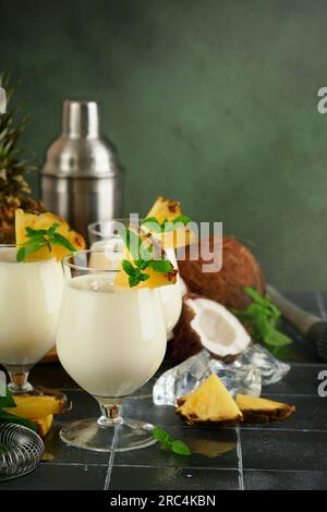 Pina Colada. Traditioneller karibischer Cocktail aus Rum, Ananassaft und Kokosnusscreme mit tropischen Früchten und Barutensilien auf frischem grünen Hintergrund. Stockfoto