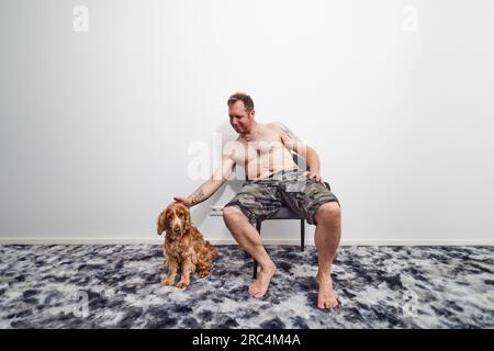 Ein Mann, der im Sommer mit Cockerspaniel auf einem Stuhl sitzt Stockfoto