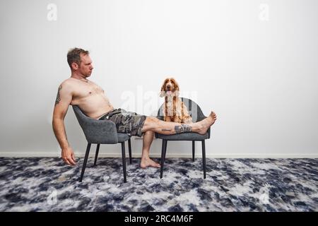 Ein Mann, der im Sommer mit Cockerspaniel auf einem Stuhl sitzt Stockfoto
