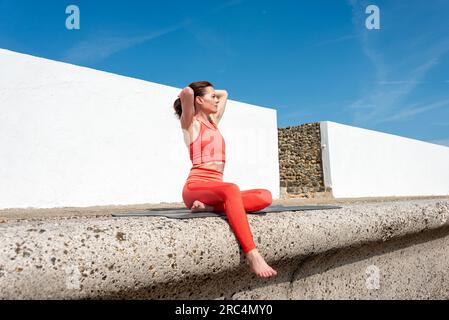 Eine Frau, die auf einer Trainingsmatte sitzt und sich draußen die Haare zusammenbindet. Stockfoto
