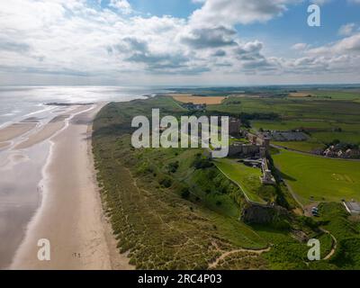 Luftdrohnenfoto von Bamburgh Castle an der wunderschönen Küste von Northumberland, England. Das Schloss ist von Dünen, Strand und Meer umgeben Stockfoto