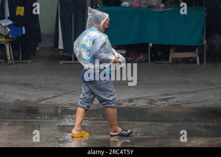 SAMUT PRAKAN, THAILAND, MAI 10 2023, Ein Taxifahrer auf einem Motorrad läuft mit einem Regenmantel und verschiedenen Schuhen eine regnerische Straße entlang Stockfoto