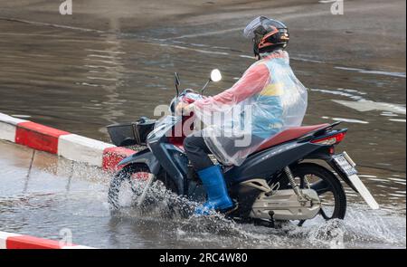 SAMUT PRAKAN, THAILAND, MAI 12 2023, Ein Fahrer des Moto-Taxis fährt durch eine Pfütze im Regen Stockfoto