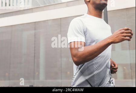 Die Seitenansicht des anonymen Crop passt dem schwarzen männlichen Athleten in Sportbekleidung beim Laufen, während er morgens in der Innenstadt der modernen Stadt trainiert Stockfoto