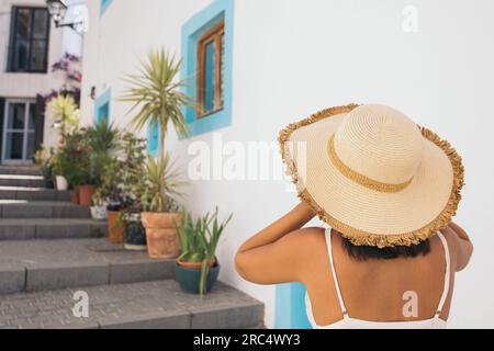 Rückblick auf eine anonyme junge Touristenfrau mit Strohhut, die während der Besichtigung des tropischen Resorts auf den Balearen im Sommer Fotos macht Stockfoto