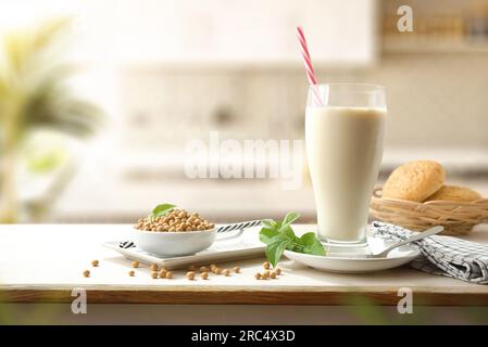 Soja-Getränk in einem großen Glas mit Sojabohnen in einem Behälter auf einer Holzbank in einer Küche. Vorderansicht. Stockfoto