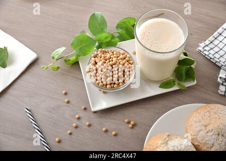 Sojamilch in einem Glas auf einem Teller mit einer Schüssel voller Sojabohnen auf einer Holzbank mit Blatt und Brotplatte. Draufsicht. Stockfoto