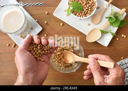 Zubereiten von Sojagetränken zu Hause mit weichen, trockenen Bohnen und verschiedenen Küchenartikeln auf einem rustikalen Holztisch. Draufsicht. Stockfoto