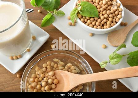 Zubereiten von Sojagetränken zu Hause mit weichen, trockenen Bohnen und verschiedenen Küchenartikeln auf einem rustikalen Holztisch. Draufsicht. Stockfoto
