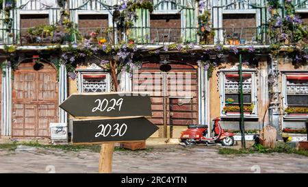Ein Bild mit einem Hinweisschild, das in zwei verschiedene Richtungen auf Deutsch zeigt. Eine Richtung zeigt auf 2029, die andere auf 2030 Stockfoto