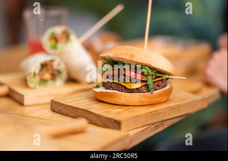 Leckerer veganer Burger mit frischen Tomatenscheiben auf einem Holzbrett auf dem Tisch mit verschwommenem Hintergrund im Restaurant Stockfoto