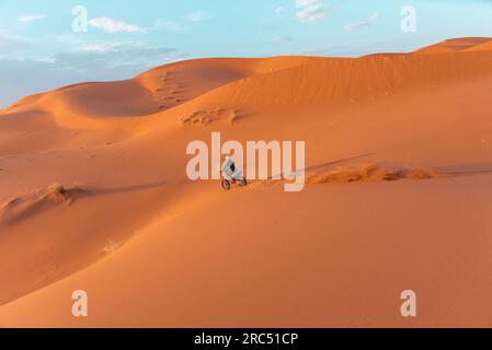 Seitenansicht einer nicht wiedererkennbaren Person, die Motorrad auf Sanddünen vor bewölktem Himmel in der Merzouga-Wüste Marokko fährt Stockfoto